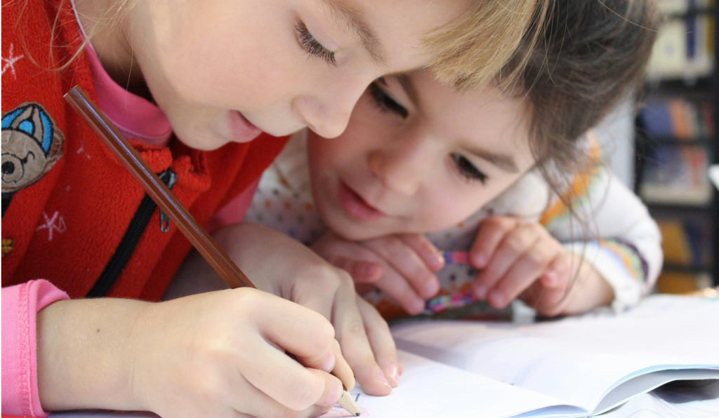 two children writing on a notebook and looking over
