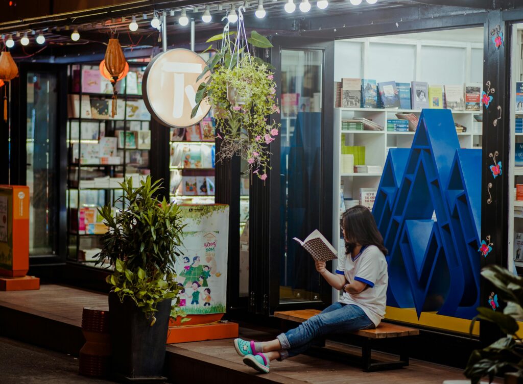 A girl sitting on a bench outside the library, reading a book.